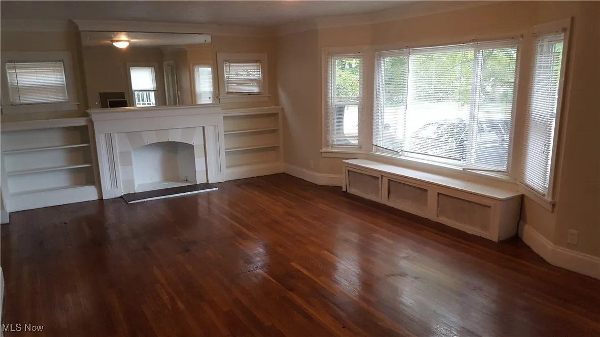 Unfurnished living room with dark wood finished floors, ornamental molding, and a tile fireplace