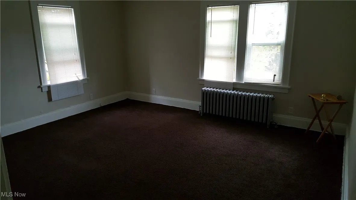 Unfurnished room with radiator heating unit, dark colored carpet, and healthy amount of natural light