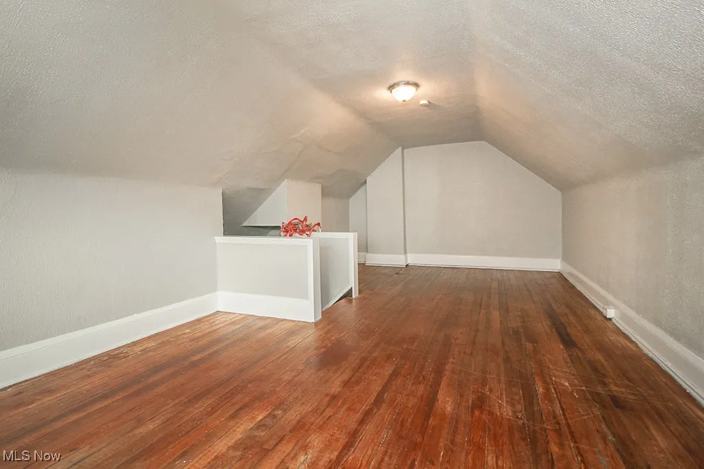 Additional living space featuring a textured ceiling, hardwood / wood-style flooring, and vaulted ceiling