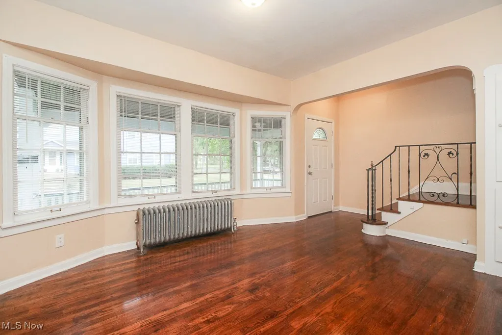 Foyer entrance featuring radiator heating unit, wood finished floors, stairway, and arched walkways