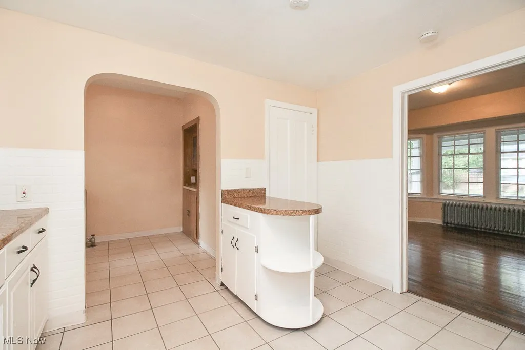 Kitchen featuring radiator heating unit, tile walls, light tile patterned floors, white cabinetry, and a wainscoted wall
