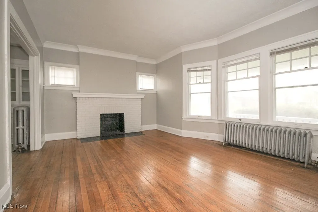 Unfurnished living room featuring radiator heating unit, hardwood / wood-style flooring, crown molding, and a fireplace