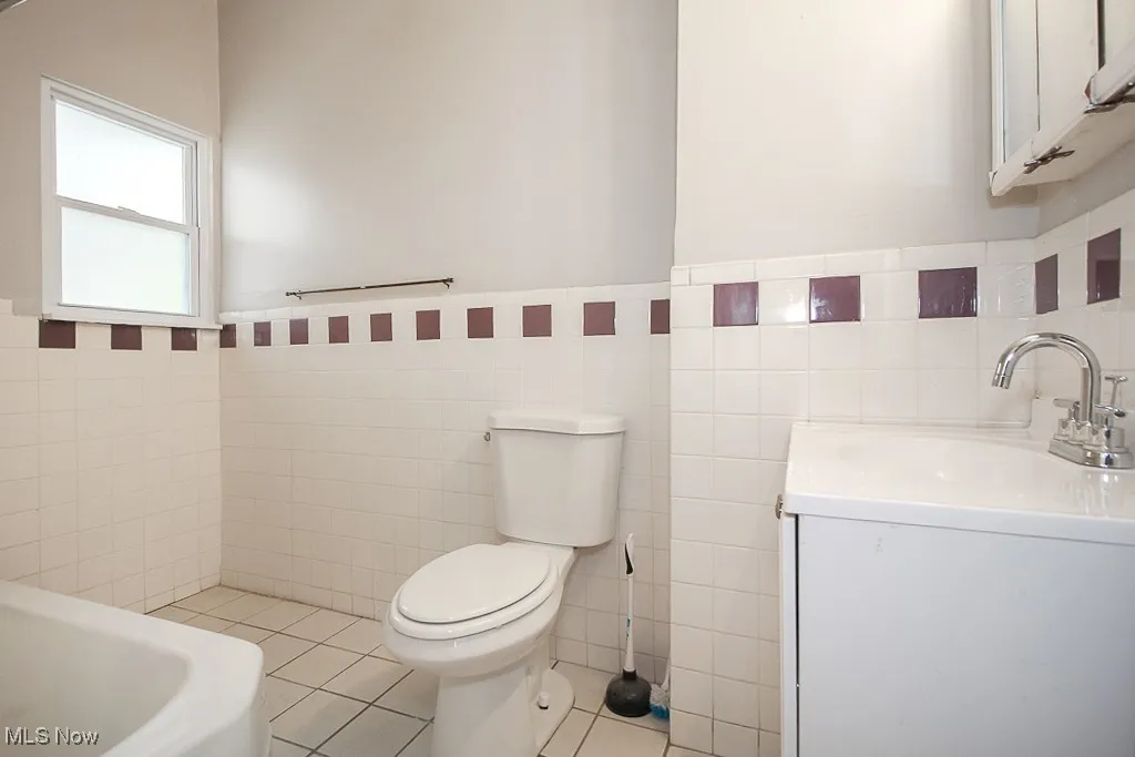 Bathroom with tile walls, tile patterned flooring, vanity, and wainscoting