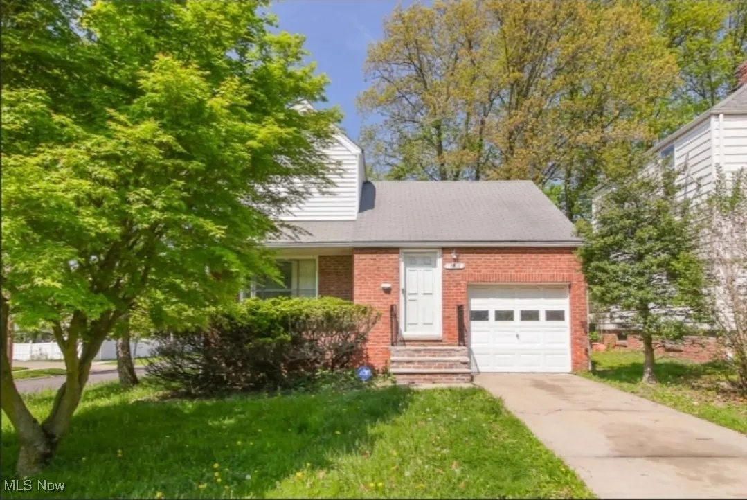 View of front of house with brick siding, driveway, a garage, and a front lawn