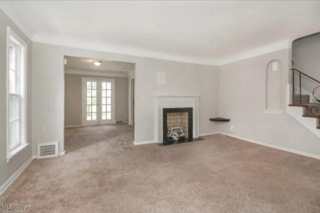 Unfurnished living room with a fireplace with flush hearth, carpet, and stairway