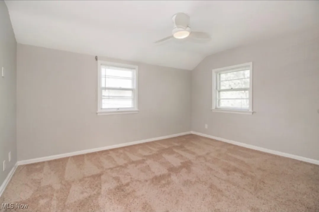 Unfurnished room with vaulted ceiling, carpet flooring, and a ceiling fan