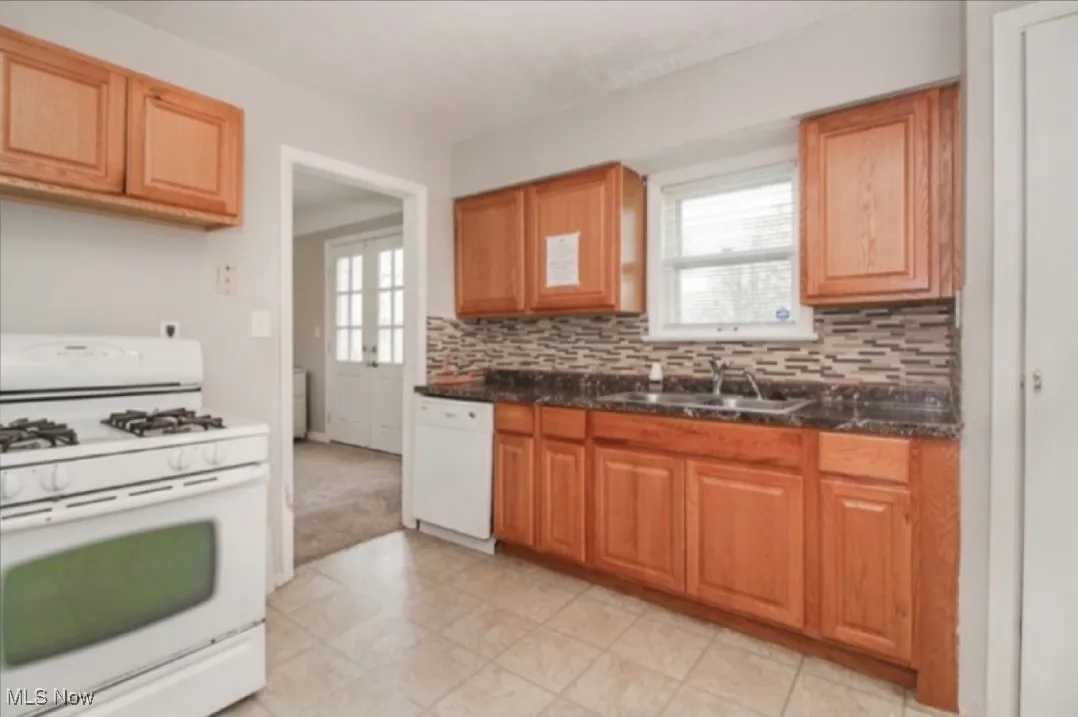 Kitchen featuring white appliances, decorative backsplash, dark countertops, and brown cabinets