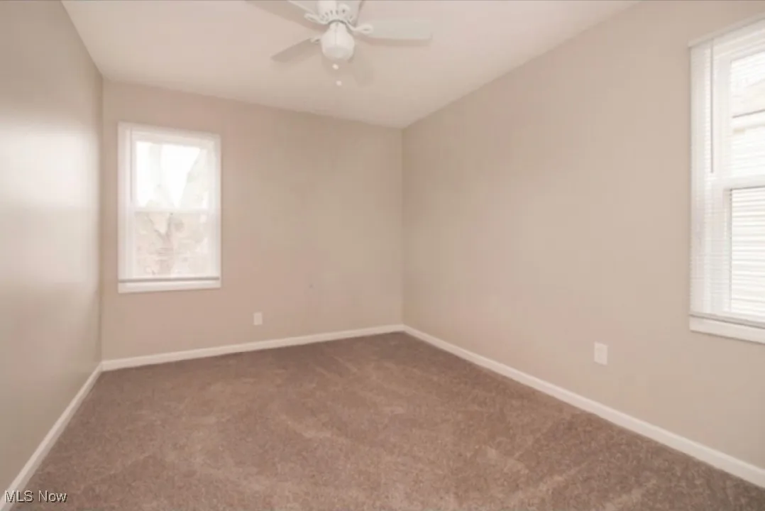 Carpeted spare room featuring ceiling fan and plenty of natural light