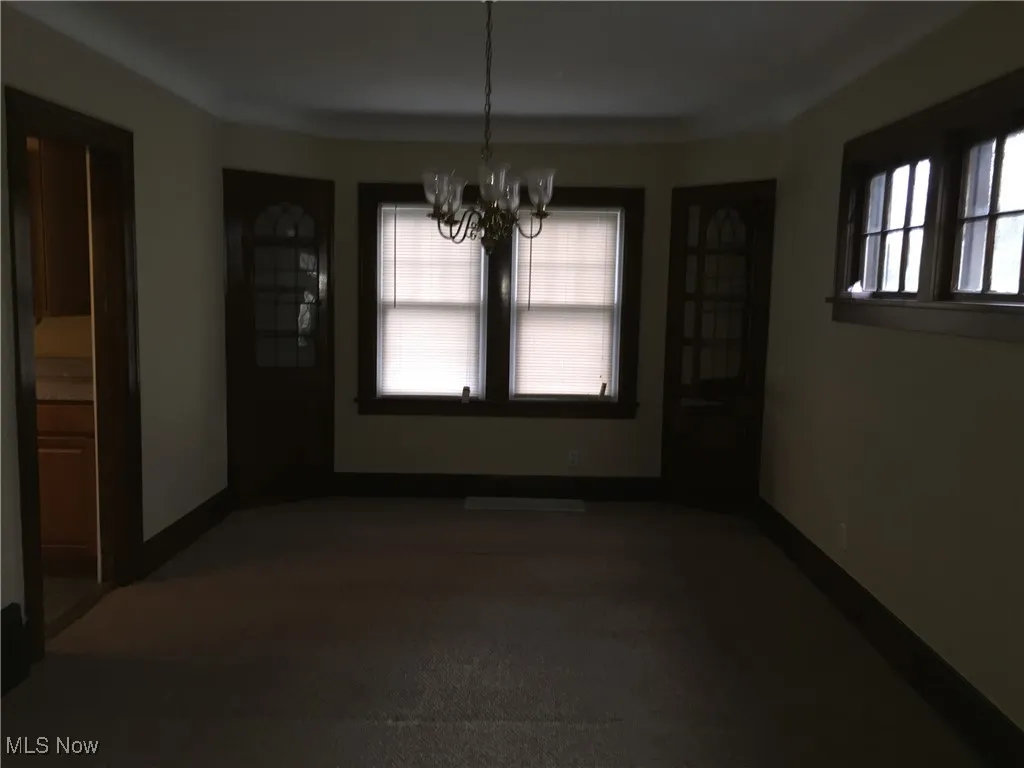 Unfurnished dining area featuring a chandelier and dark carpet