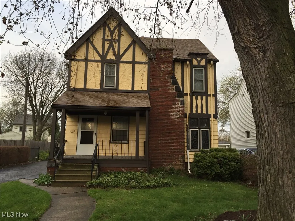 Tudor home with covered porch and roof with shingles