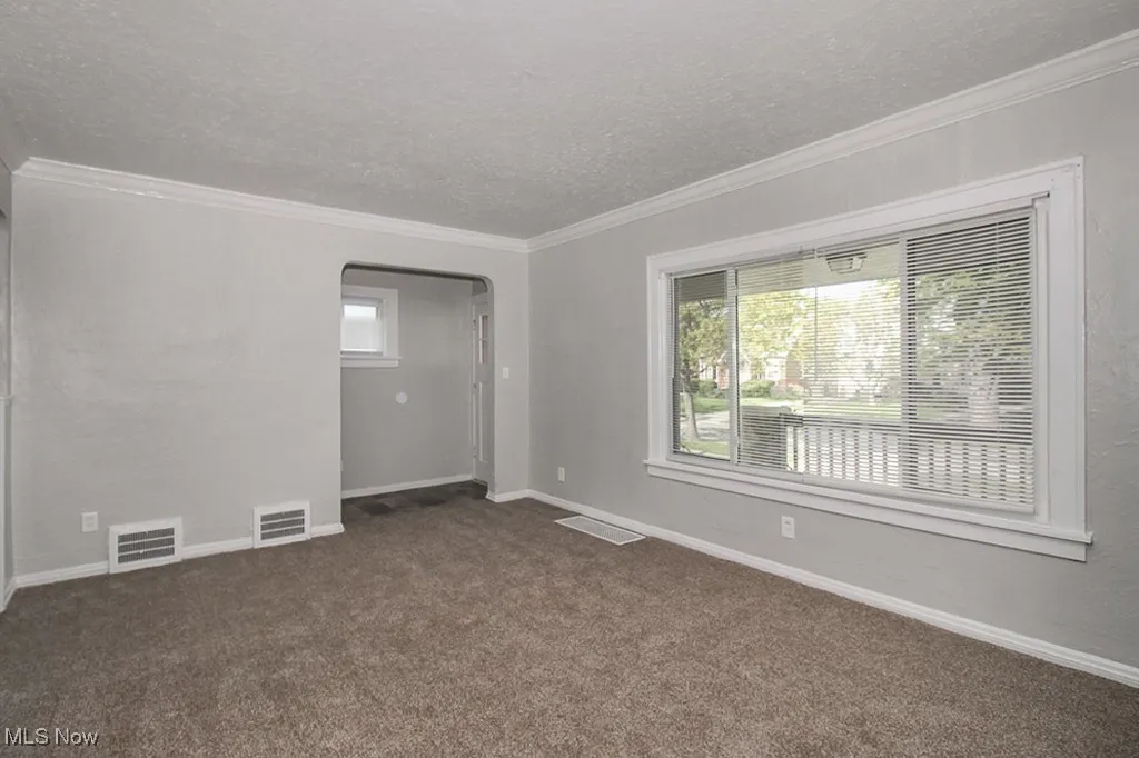 Unfurnished room with a textured ceiling, ornamental molding, healthy amount of natural light, dark colored carpet, and arched walkways