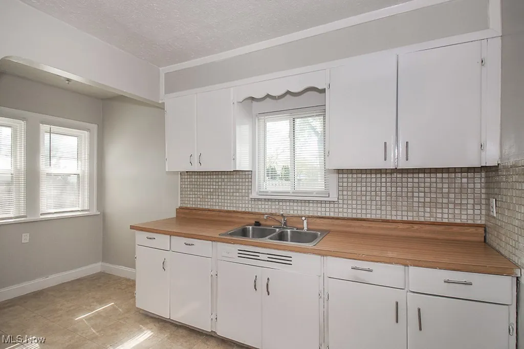 Kitchen with decorative backsplash, white cabinetry, butcher block countertops, and a textured ceiling