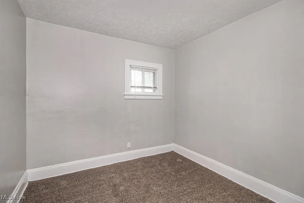 Empty room featuring a textured ceiling and dark colored carpet