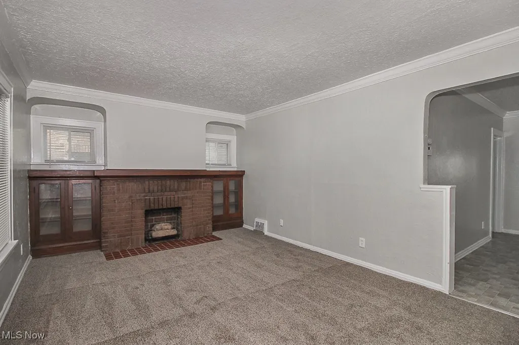 Unfurnished living room with arched walkways, a textured ceiling, carpet floors, a brick fireplace, and ornamental molding