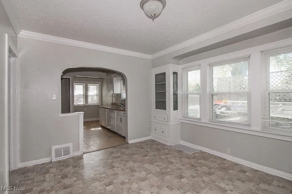 Unfurnished dining area with arched walkways, stone finish flooring, a textured ceiling, and ornamental molding
