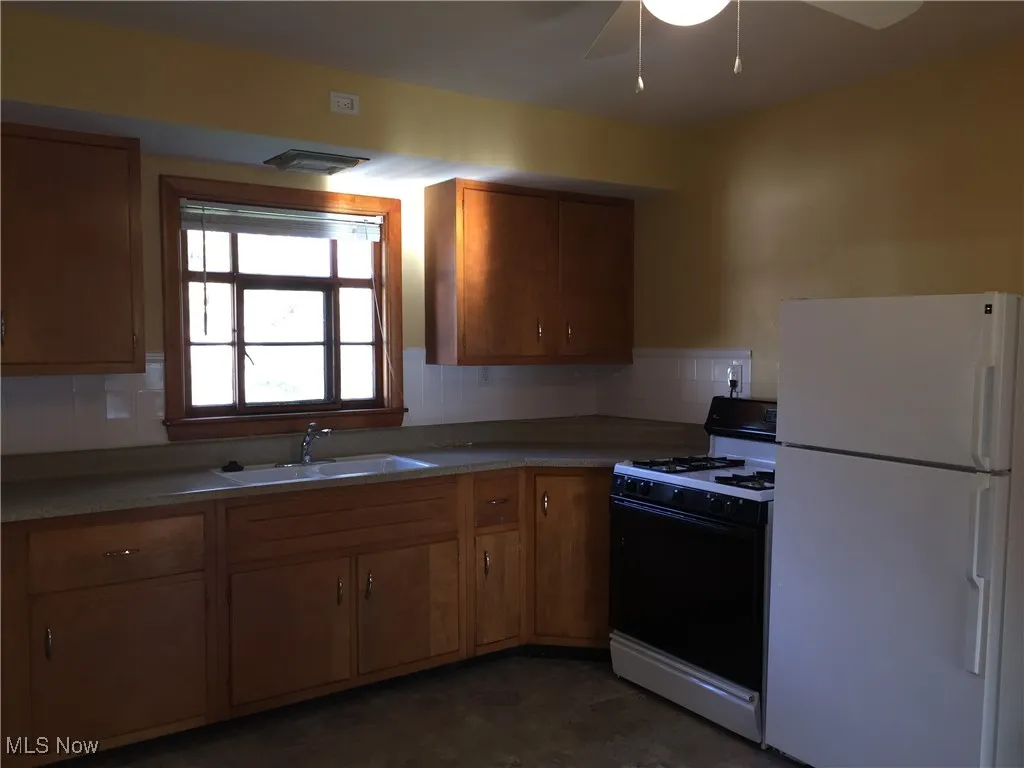 Kitchen with white appliances, brown cabinetry, tasteful backsplash, a ceiling fan, and light countertops