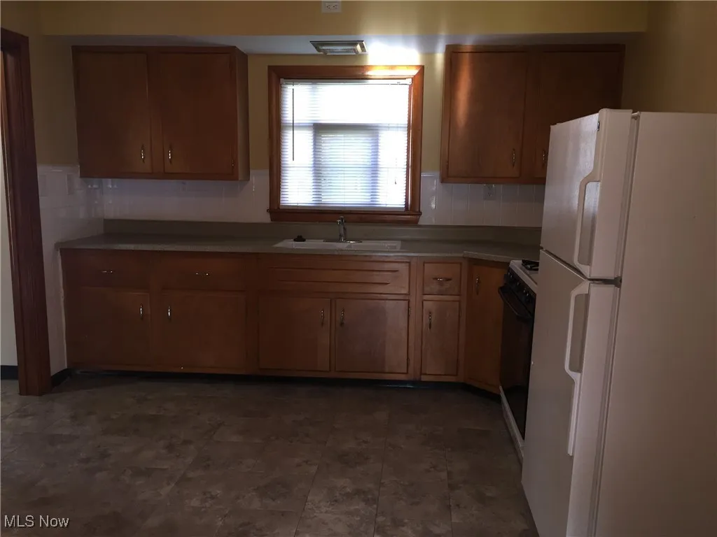 Kitchen with freestanding refrigerator, range, brown cabinets, and backsplash