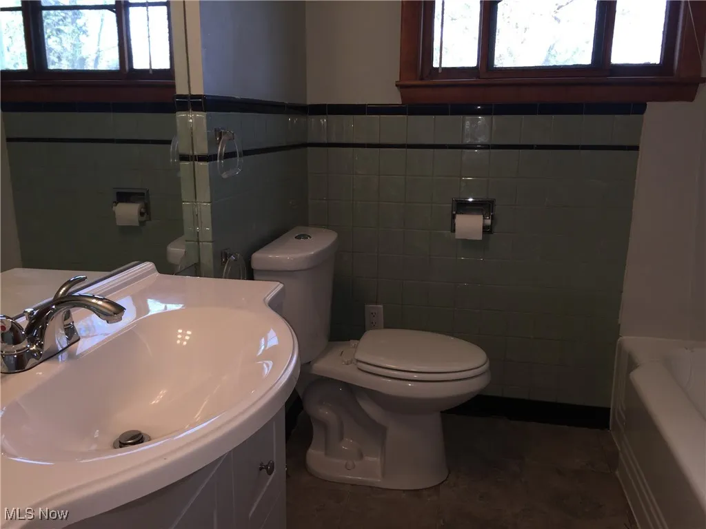 Bathroom featuring tile walls, a tub, vanity, and a wainscoted wall