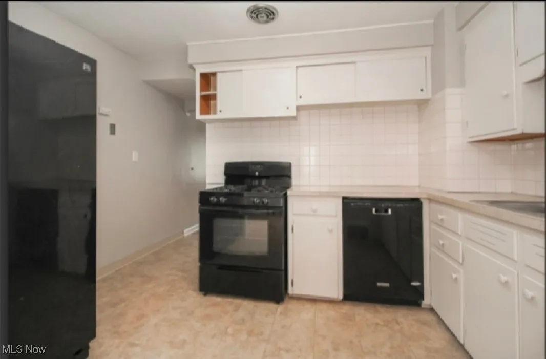 Kitchen featuring black appliances, light countertops, decorative backsplash, and white cabinets