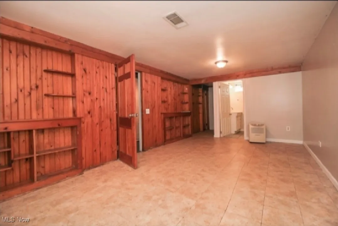Unfurnished living room featuring wood walls and baseboards