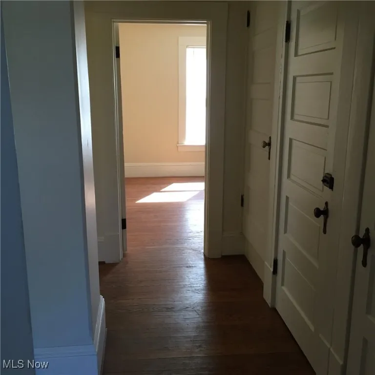 Hallway featuring dark wood-style floors and baseboards