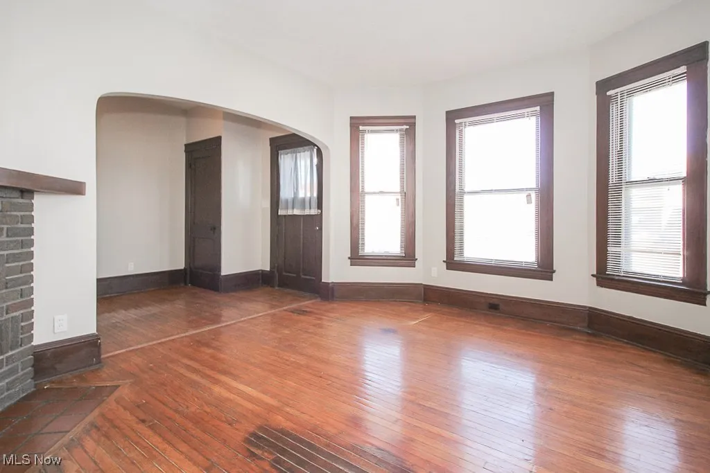 Unfurnished living room featuring wood-type flooring, arched walkways, and plenty of natural light