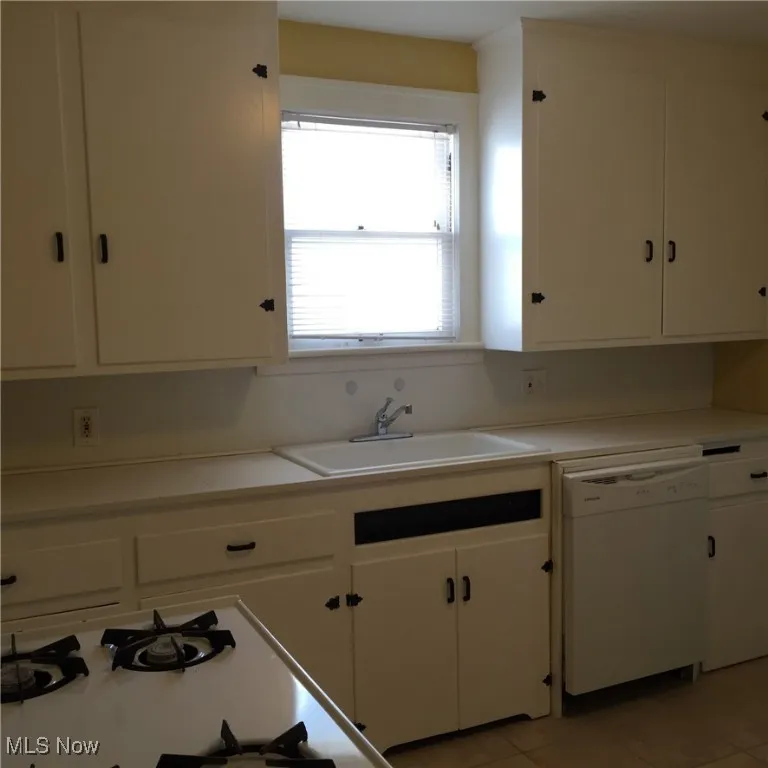 Kitchen featuring white appliances, white cabinets, light countertops, and light tile patterned flooring