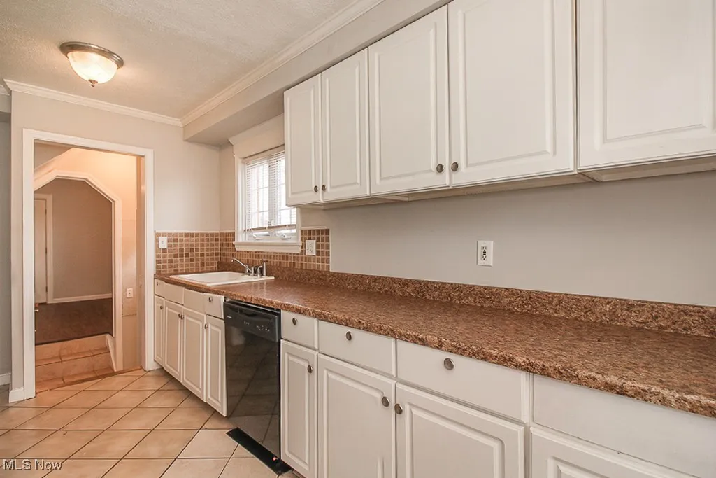Kitchen with dishwasher, white cabinetry, light tile patterned flooring, crown molding, and dark countertops