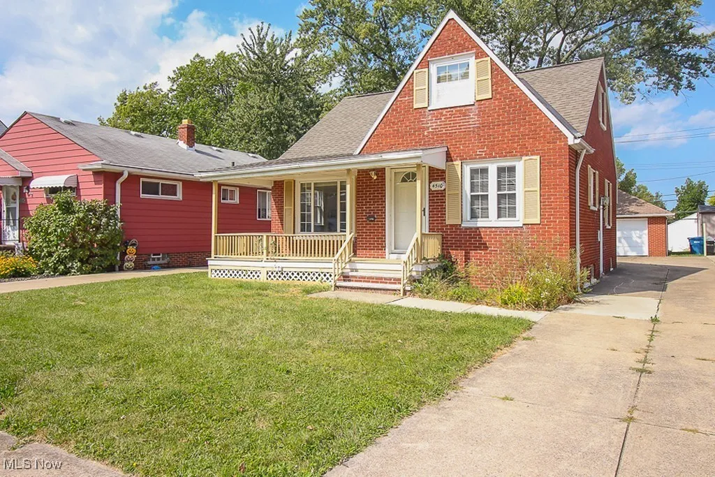 View of front of home featuring brick siding, a porch, a shingled roof, a front yard, and an outdoor structure