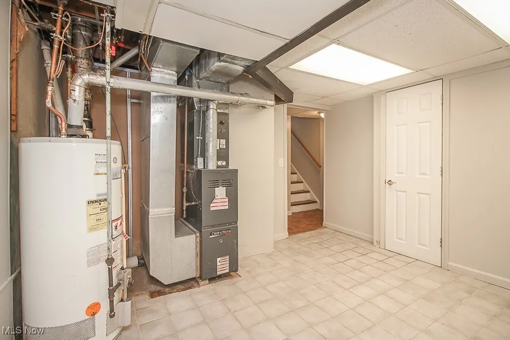 Finished basement with water heater, stairway, tile patterned floors, and heating unit