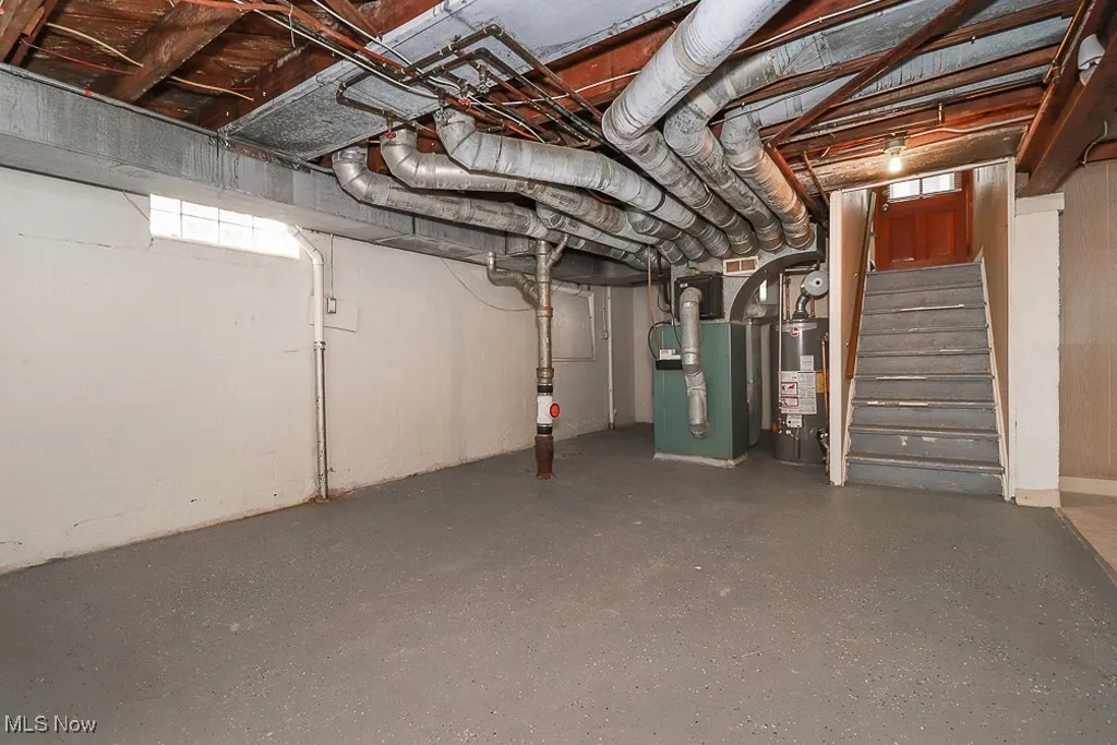 Unfinished below grade area with gas water heater, stairs, and heating unit