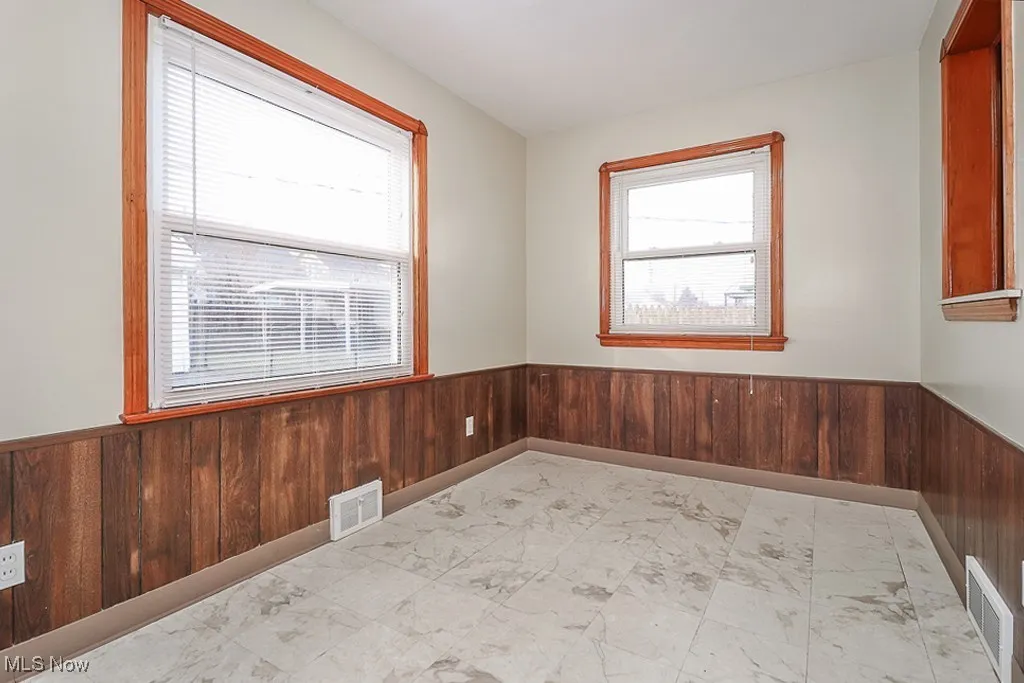 Empty room featuring wainscoting, wooden walls, and marble finish flooring