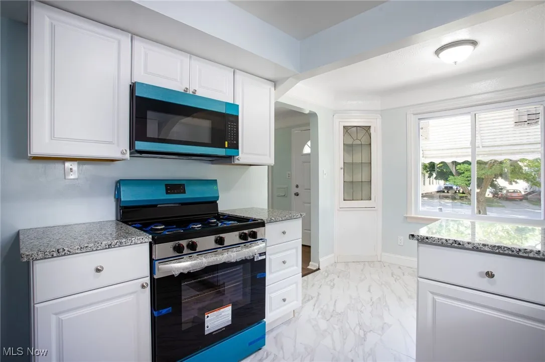 Kitchen with stainless steel gas stove, light marble finish floors, light stone countertops, white cabinetry, and arched walkways