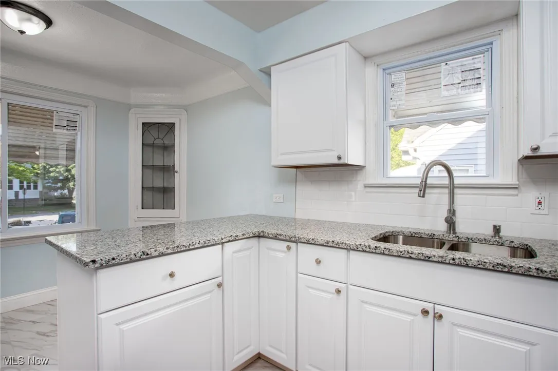 Kitchen with white cabinets, light marble finish flooring, light stone countertops, decorative backsplash, and a peninsula