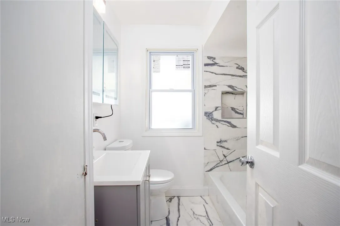 Bathroom featuring marble finish flooring, vanity, and washtub / shower combination