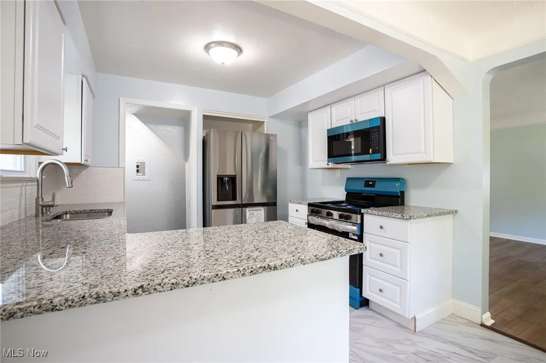 Kitchen with stainless steel appliances, light stone counters, a peninsula, white cabinetry, and backsplash