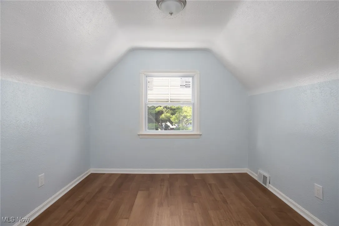 Additional living space with dark wood-type flooring, vaulted ceiling, and a textured ceiling