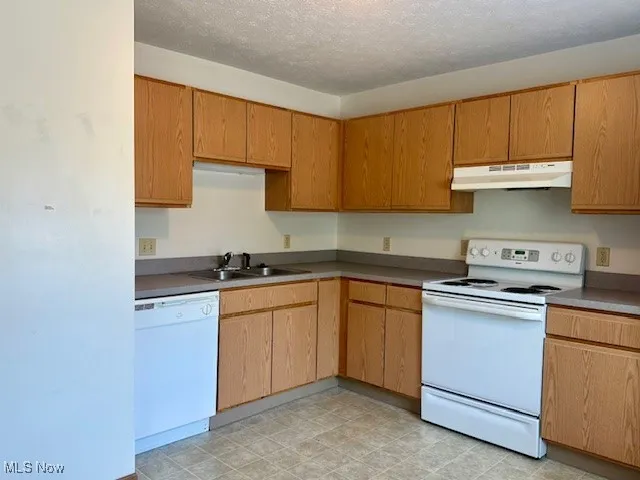 Kitchen with white appliances, under cabinet range hood, and a textured ceiling