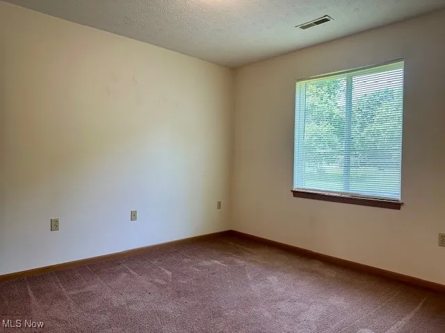 Carpeted empty room featuring baseboards and a textured ceiling