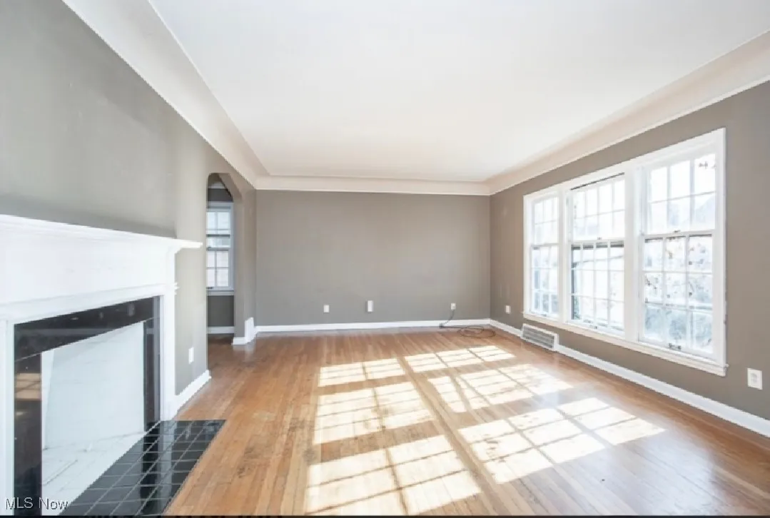 Unfurnished living room featuring wood finished floors, a tiled fireplace, and arched walkways
