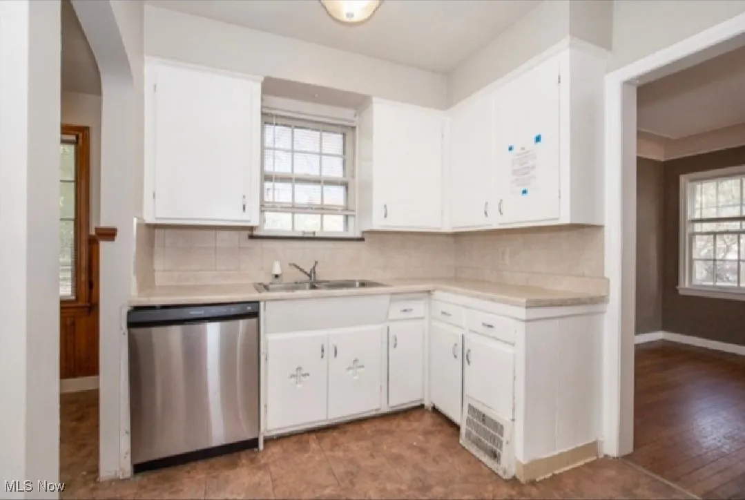 Kitchen with stainless steel dishwasher, light countertops, and white cabinetry