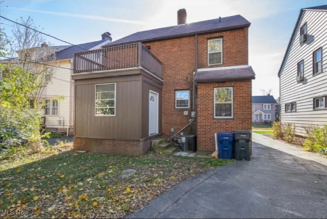 Back of property with entry steps, a balcony, brick siding, and a chimney