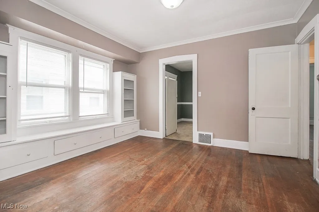 Empty room with dark wood-style floors and ornamental molding