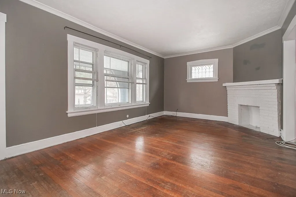 Unfurnished living room featuring hardwood / wood-style flooring, crown molding, and a brick fireplace