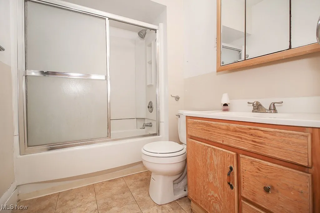Bathroom with vanity, bath / shower combo with glass door, and tile patterned flooring