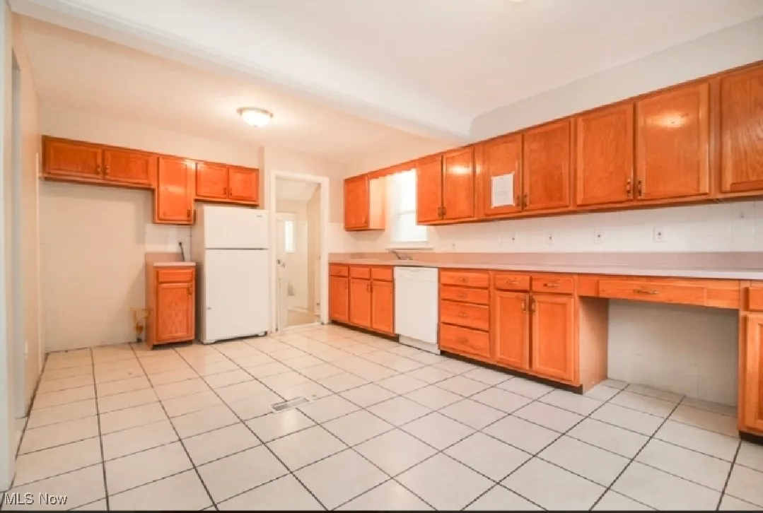 Kitchen with white appliances, built in study area, light countertops, brown cabinetry, and light tile patterned flooring