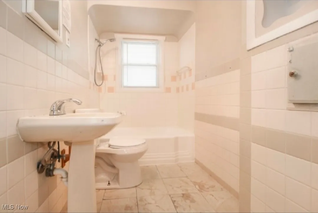 Bathroom featuring tile walls, bathing tub / shower combination, and marble look tile flooring