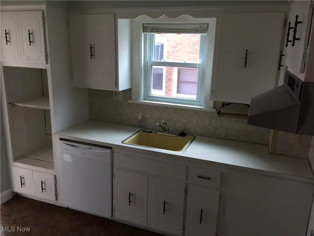 Kitchen with white dishwasher, decorative backsplash, white cabinets, and light countertops