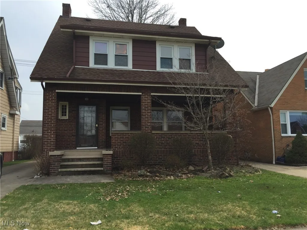 View of front of home featuring a chimney, brick siding, a front lawn, covered porch, and roof with shingles