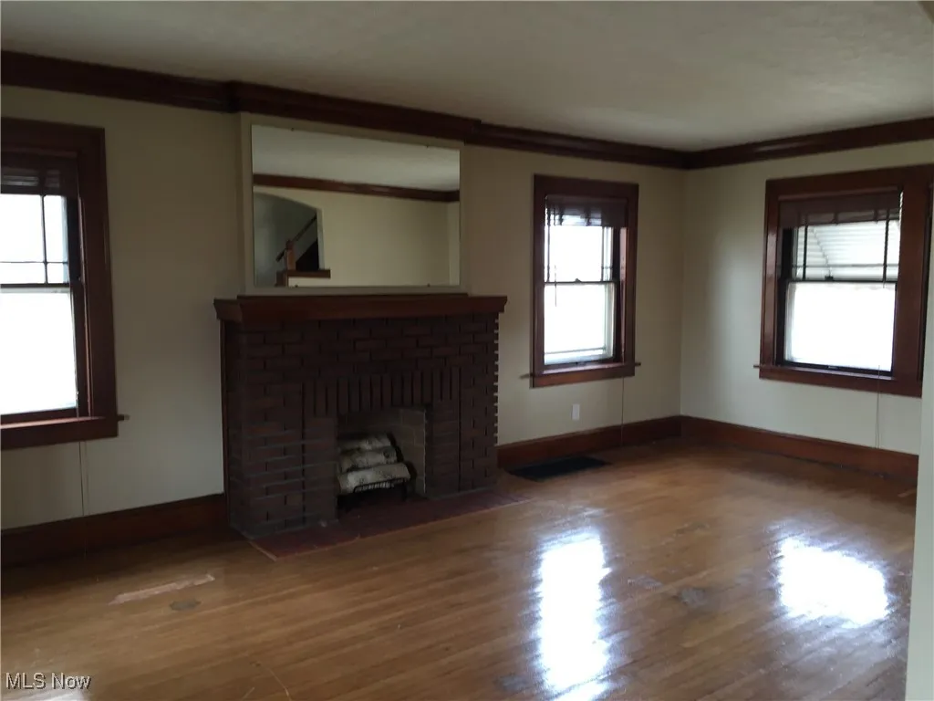 Unfurnished living room with wood finished floors, a brick fireplace, and ornamental molding